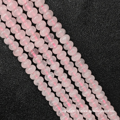 Angled view of natural rose quartz smooth disc gemstone strands arranged parallel on dark background
