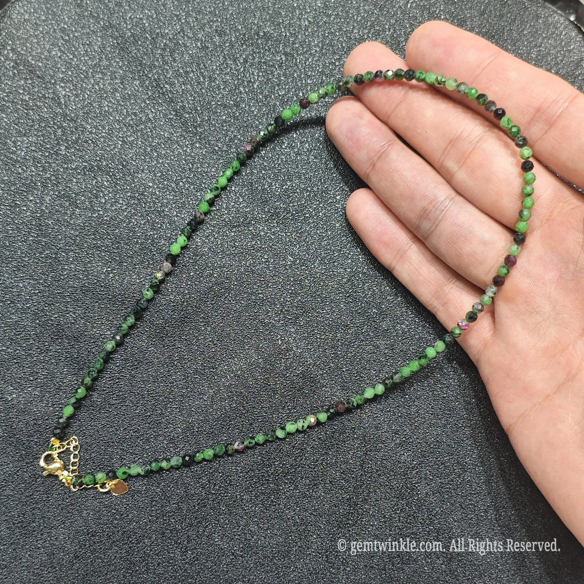 Hand holding 3mm micro faceted Ruby in Zoisite necklace strand showing green zoisite and red ruby contrast