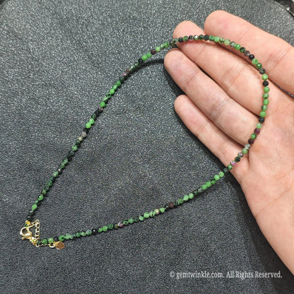 Hand holding 3mm micro faceted Ruby in Zoisite necklace strand showing green zoisite and red ruby contrast