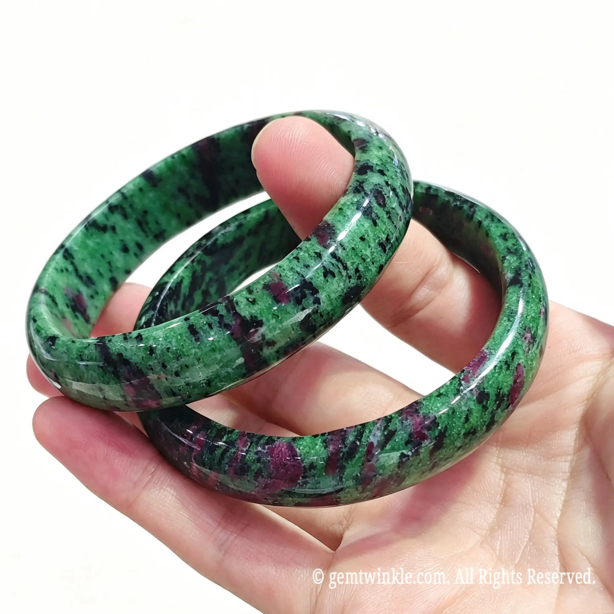 Pair of smooth round ruby in zoisite gemstone bangles held in hand showing rich red and green color contrast