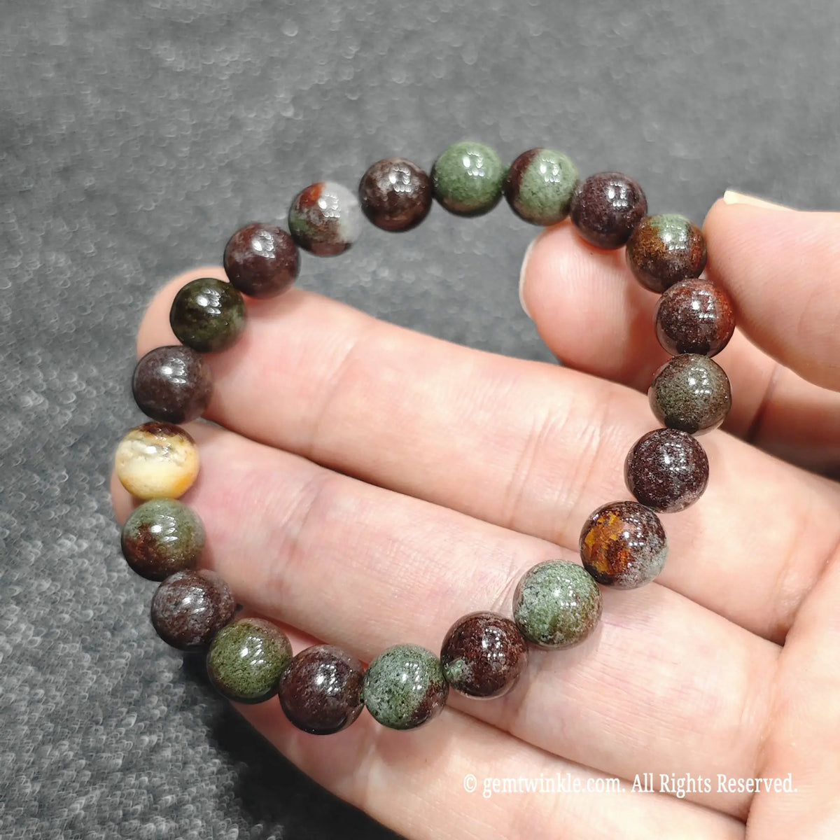 Full circle view of a classic mine green phantom quartz bracelet resting on hand over dark surface