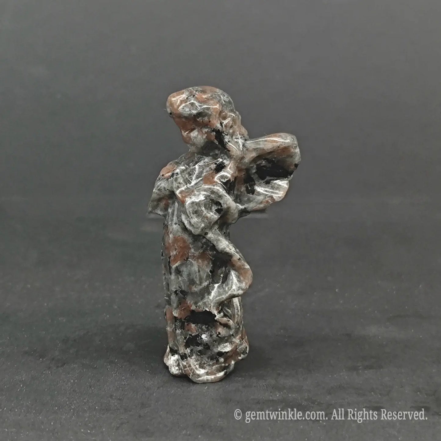Side view of a hand-carved natural granite stone angel figurine showing detailed wing curves and organic speckled mineral textures