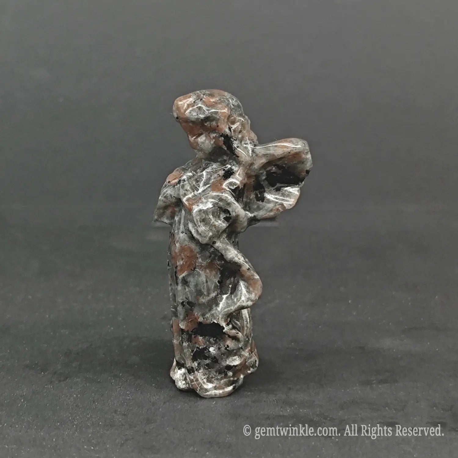 Side view of a hand-carved natural granite stone angel figurine showing detailed wing curves and organic speckled mineral textures