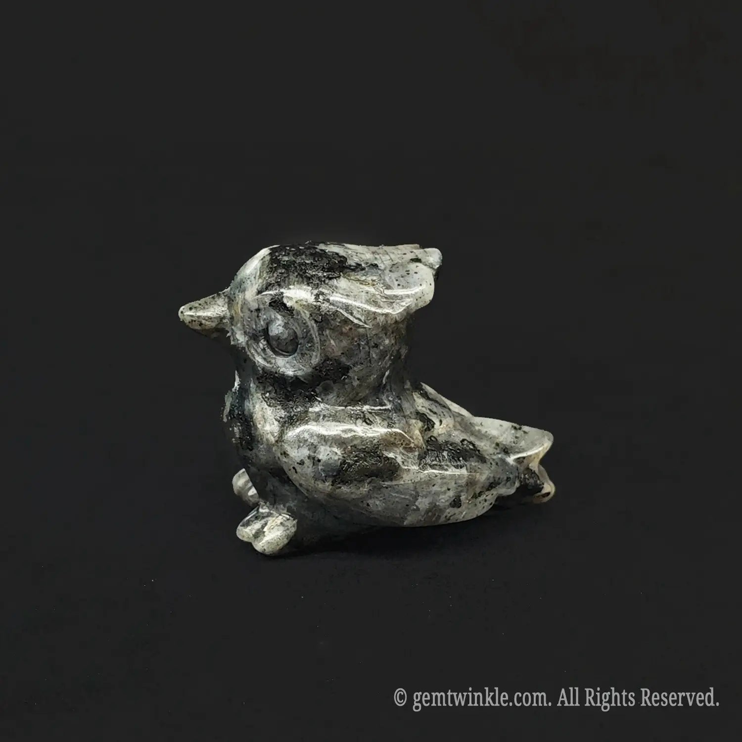 Side profile view of a rustic spotted grey stone miniature owl figurine showcasing natural dark speckled ash matrix and detailed hand carved eyes