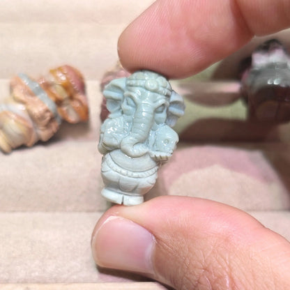 sage green natural stone ganesha statue mini figurine close up held in fingers displaying smooth polished surface