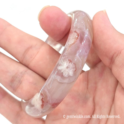 Vertical perspective of one of a kind cherry blossom agate bangle held gently between fingers highlighting flower clarity