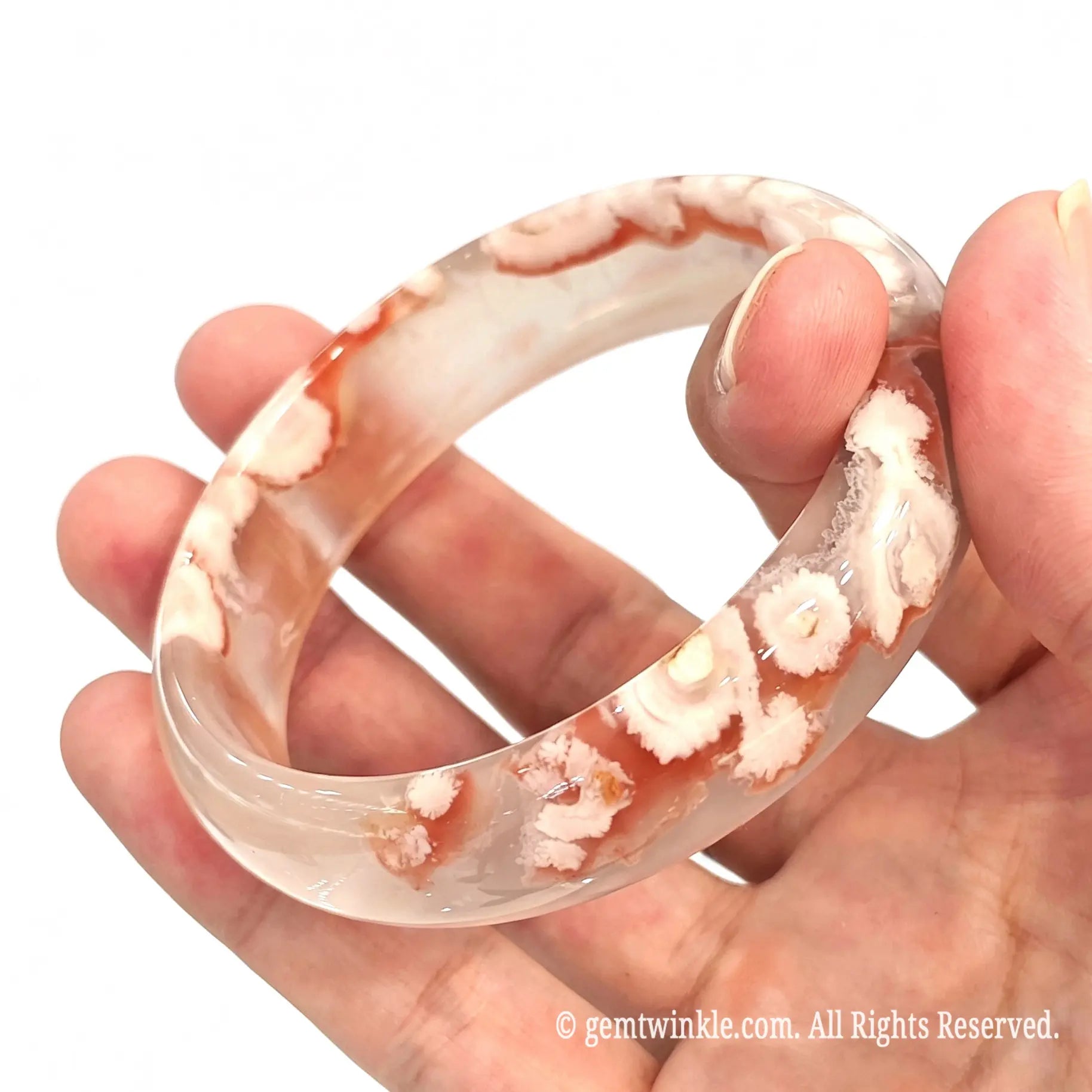 Vertical handheld perspective of one of a kind cherry blossom agate bangle held gently between fingers