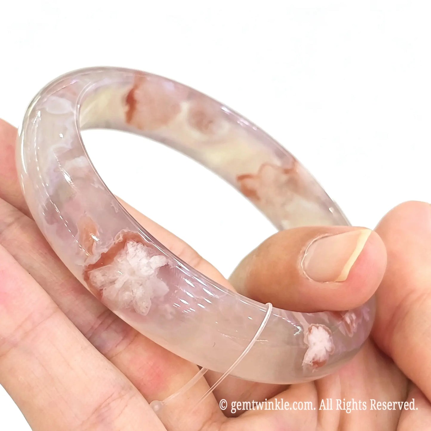 Side angle view of natural sakura agate bangle held in fingers showing band curvature and clear floral plumes