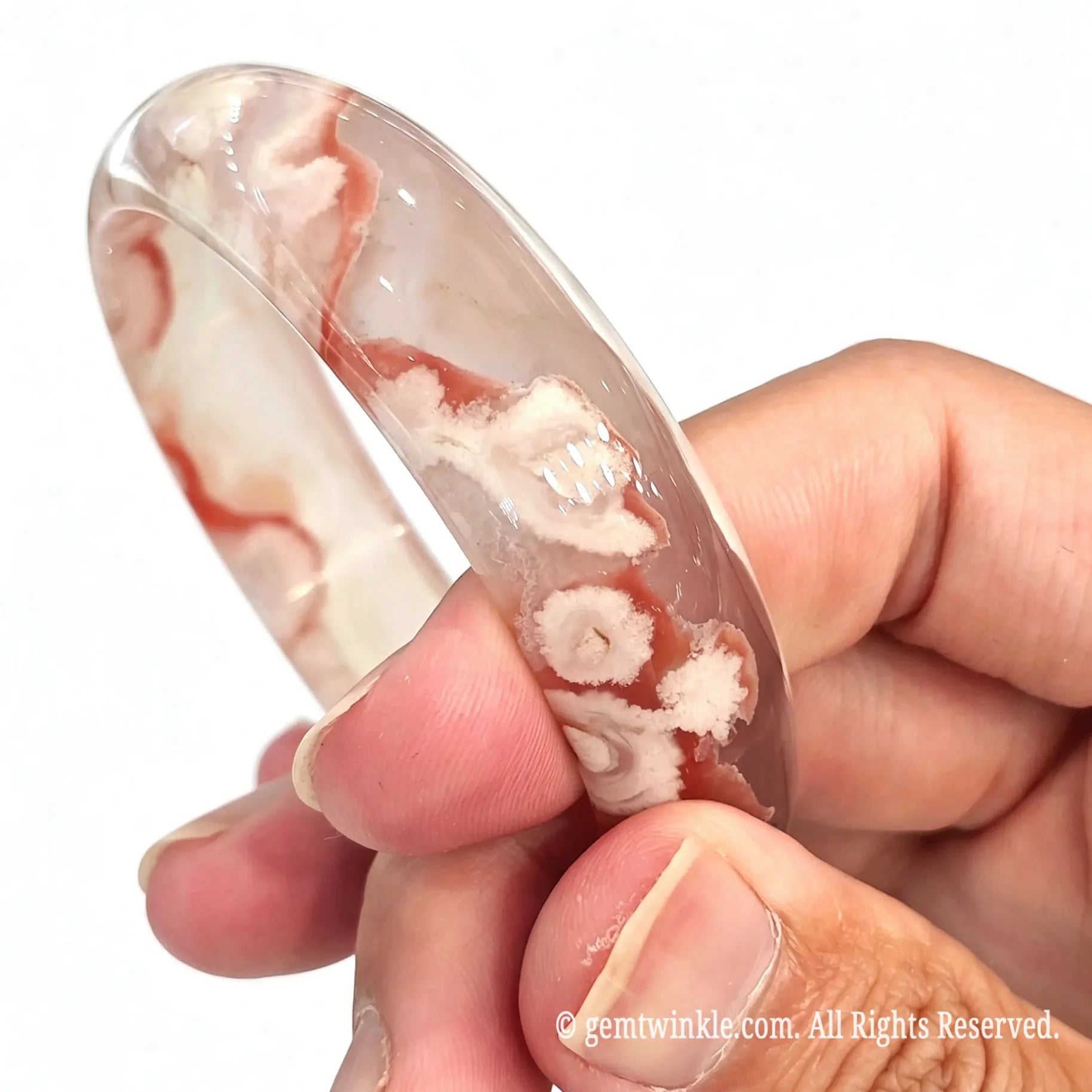 Side angle view of natural sakura agate bangle held in fingers showing band curvature and red flower patterns