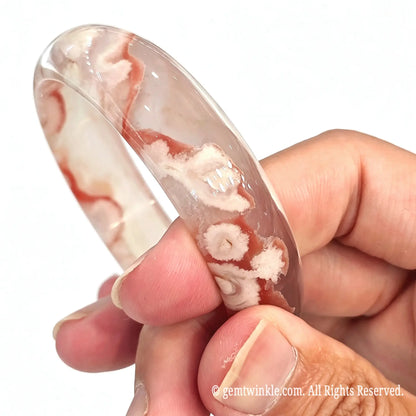 Side angle view of natural sakura agate bangle held in fingers showing band curvature and red flower patterns