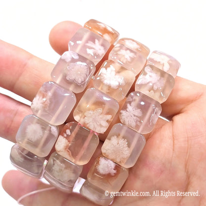 Horizontal perspective of stacked sakura agate square bead bracelets displayed on hand