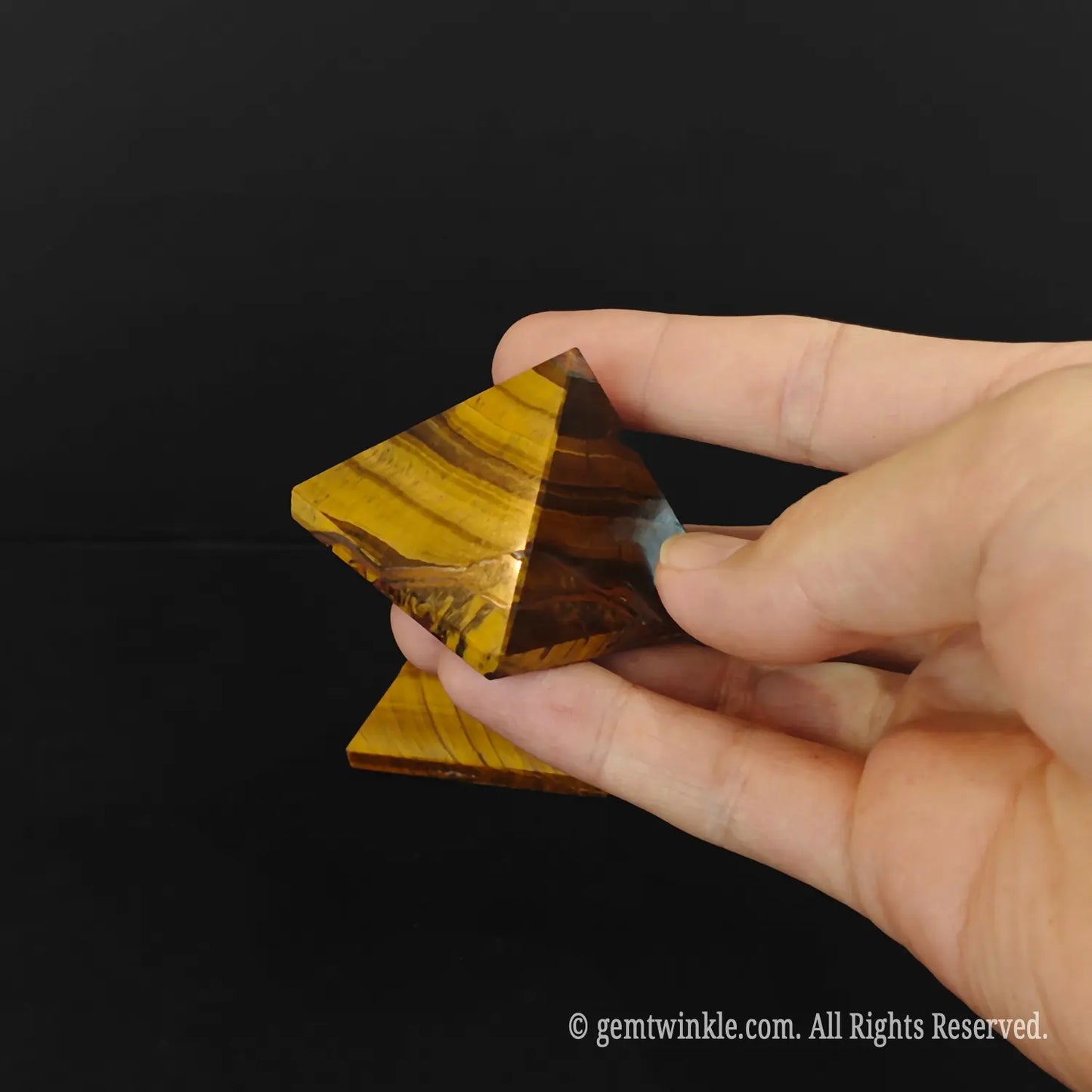 Demonstrating the separable interlocking pieces of a 4cm gold tigers eye pyramid totem