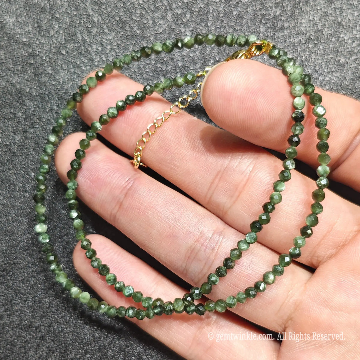 Detailed view of 3mm micro faceted seraphinite beads looped around hand with gold lobster clasp