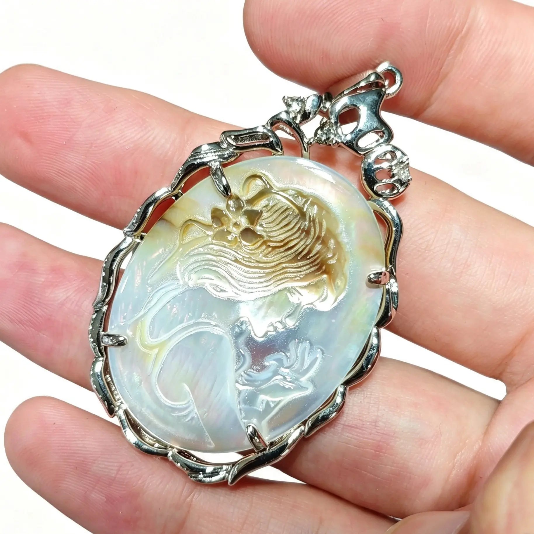 Angled view of gray shell cameo pendant held in hand showing delicate relief details and iridescent silver luster