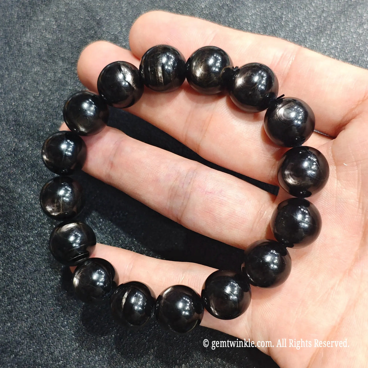 Fingertips holding a silver sheen hypersthene gemstone wristlet showing silky metallic reflections under light