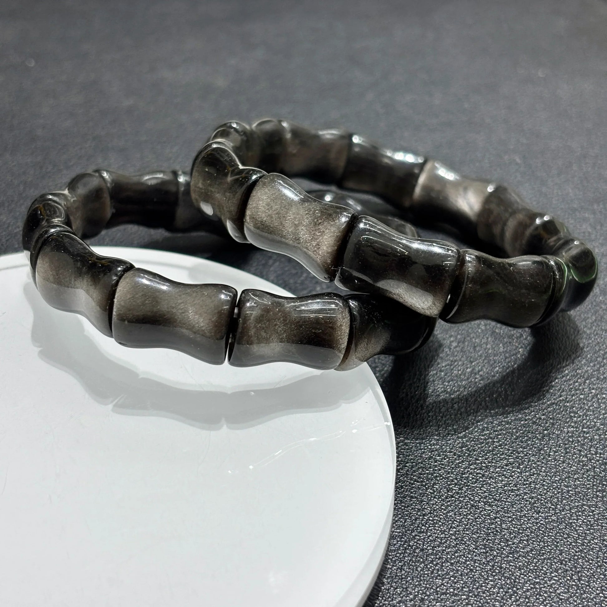 Silver Sheen Obsidian Bamboo Bead Bracelet displayed on a white stand, showing the full 18cm circumference and stretchy elastic cord.