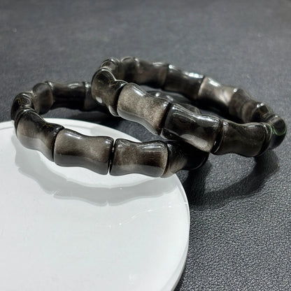 Silver Sheen Obsidian Bamboo Bead Bracelet displayed on a white stand, showing the full 18cm circumference and stretchy elastic cord.