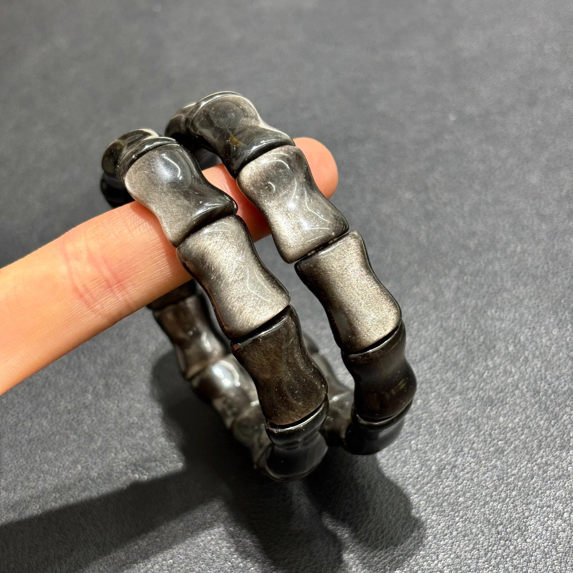Side view of the Silver Sheen Obsidian Bamboo Bead Bracelet worn on a finger, demonstrating the fit and flexibility of the stretch band.