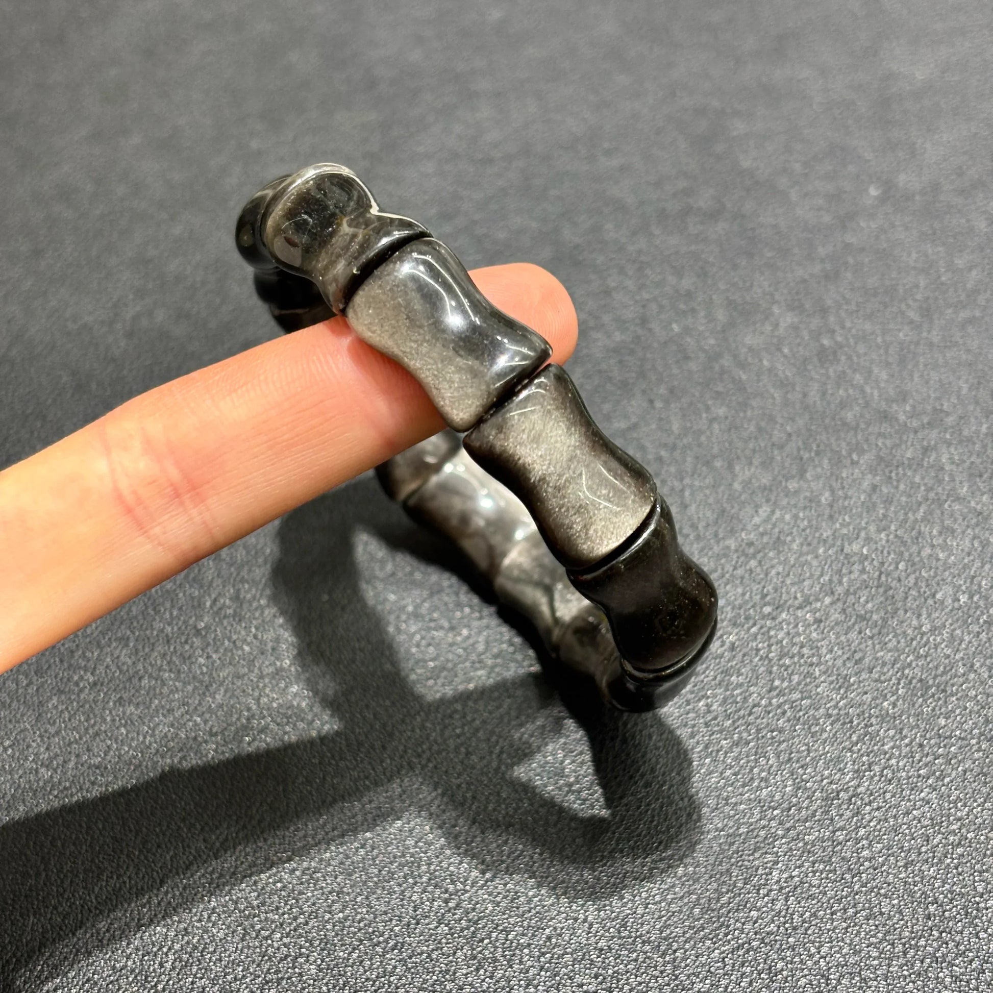 Close-up of a hand wearing the Silver Sheen Obsidian Bamboo Bracelet, highlighting the 12mm x 17mm bead size and unique texture.