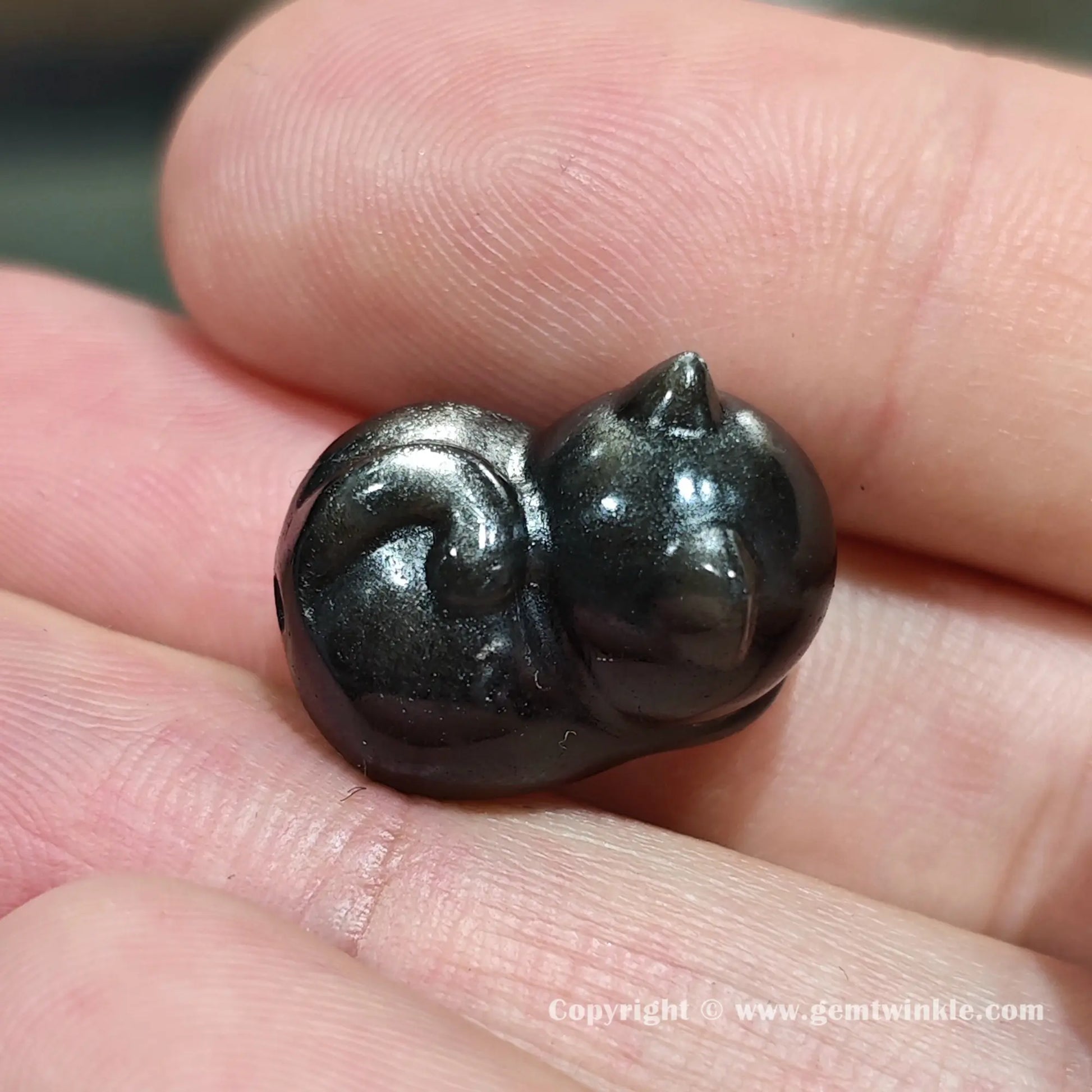 Handheld view of natural silver sheen obsidian kitten bead showcasing the side profile and glossy polished finish
