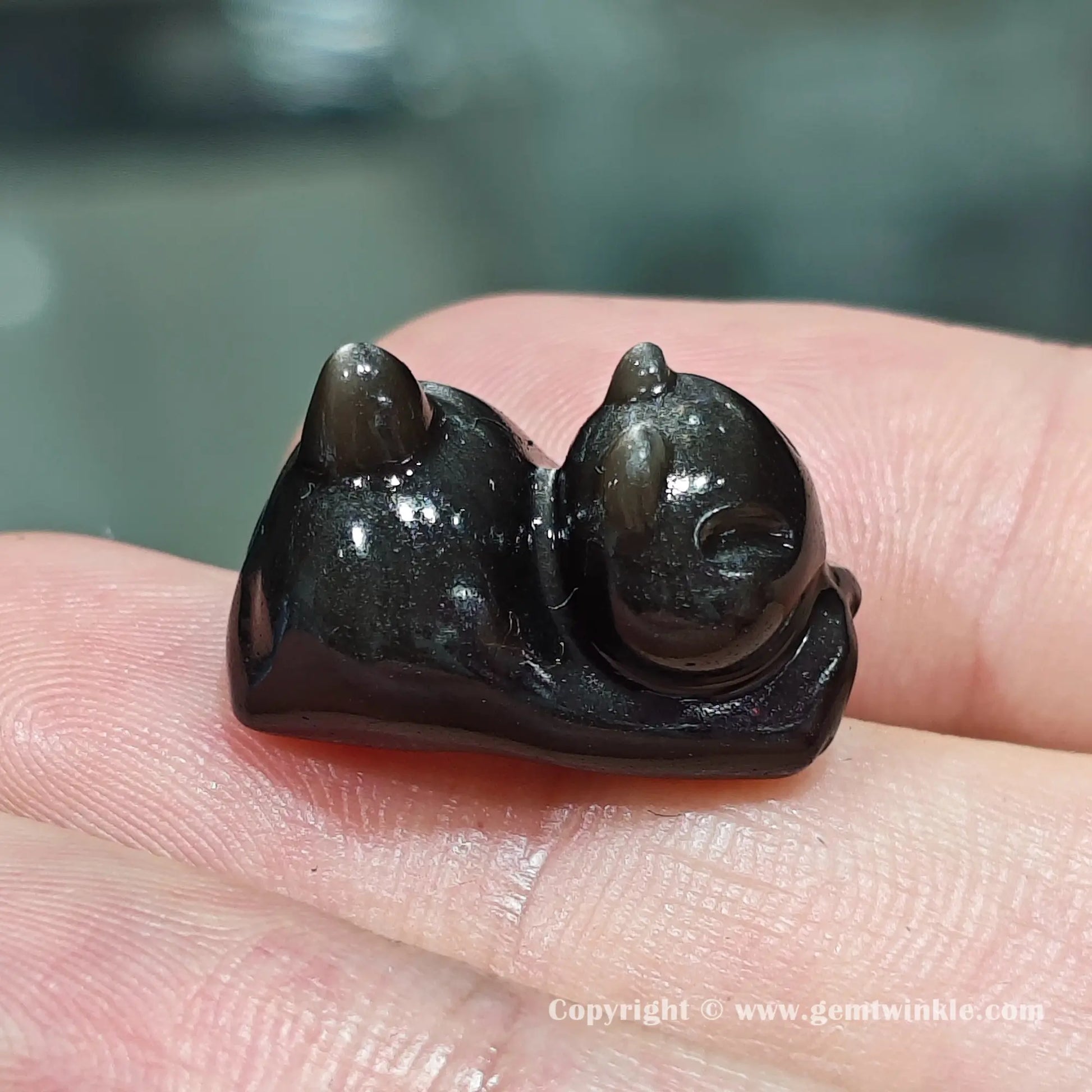 Handheld side view of natural silver sheen obsidian lazy kitten bead showcasing its glossy polished finish on hand