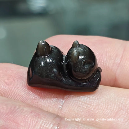 Handheld side view of natural silver sheen obsidian lazy kitten bead showcasing its glossy polished finish on hand