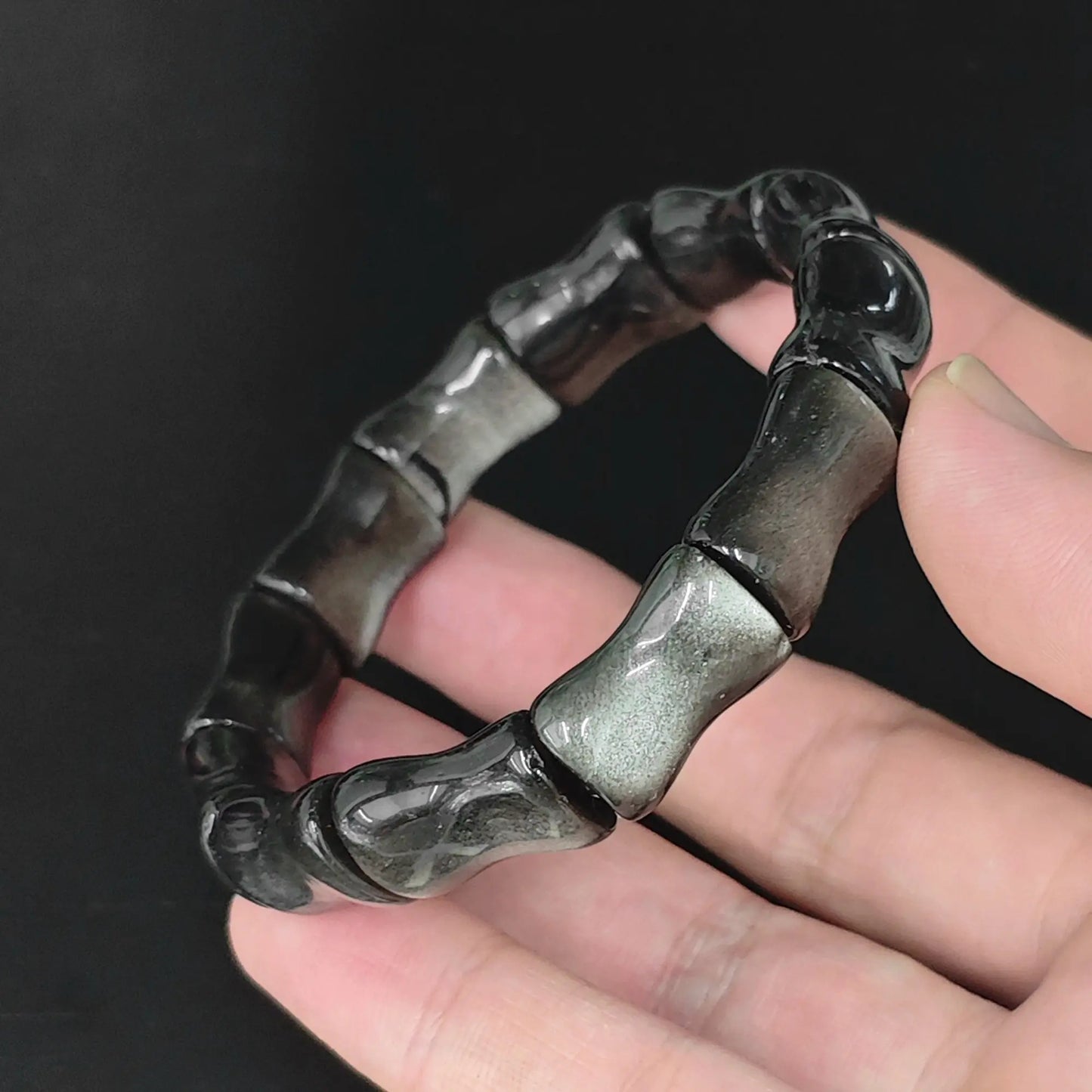 Angle view of silver sheen obsidian carved bamboo segment stretch bracelet highlighting contoured surface finish