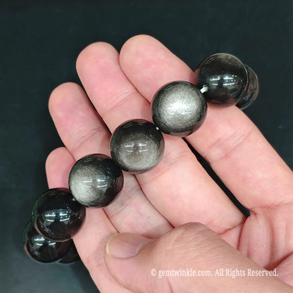 Silver sheen obsidian round bead bracelet 17-18cm held in hand showcasing reflective cat's eye optical effect