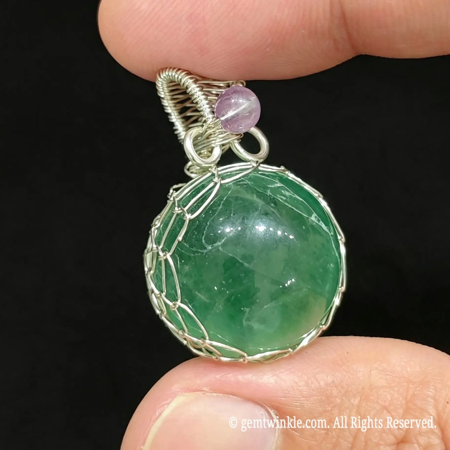 Front view of silver wire wrapped green fluorite sphere pendant held in hand showing intricate net structure