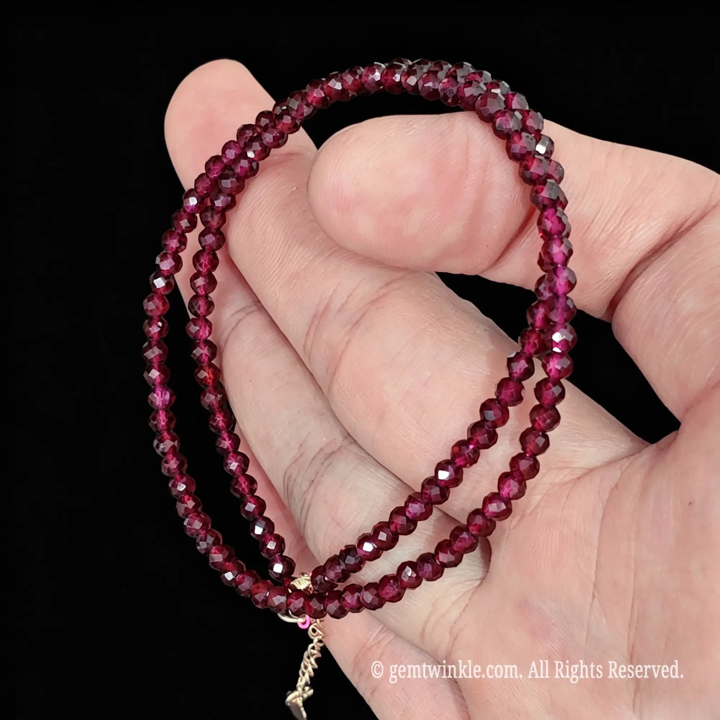 single strand red garnet choker necklace coiled across palm displaying faceted shine