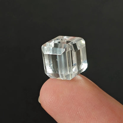Single clear quartz faceted square bead resting on fingertip showing smooth polished surface and geometric edges
