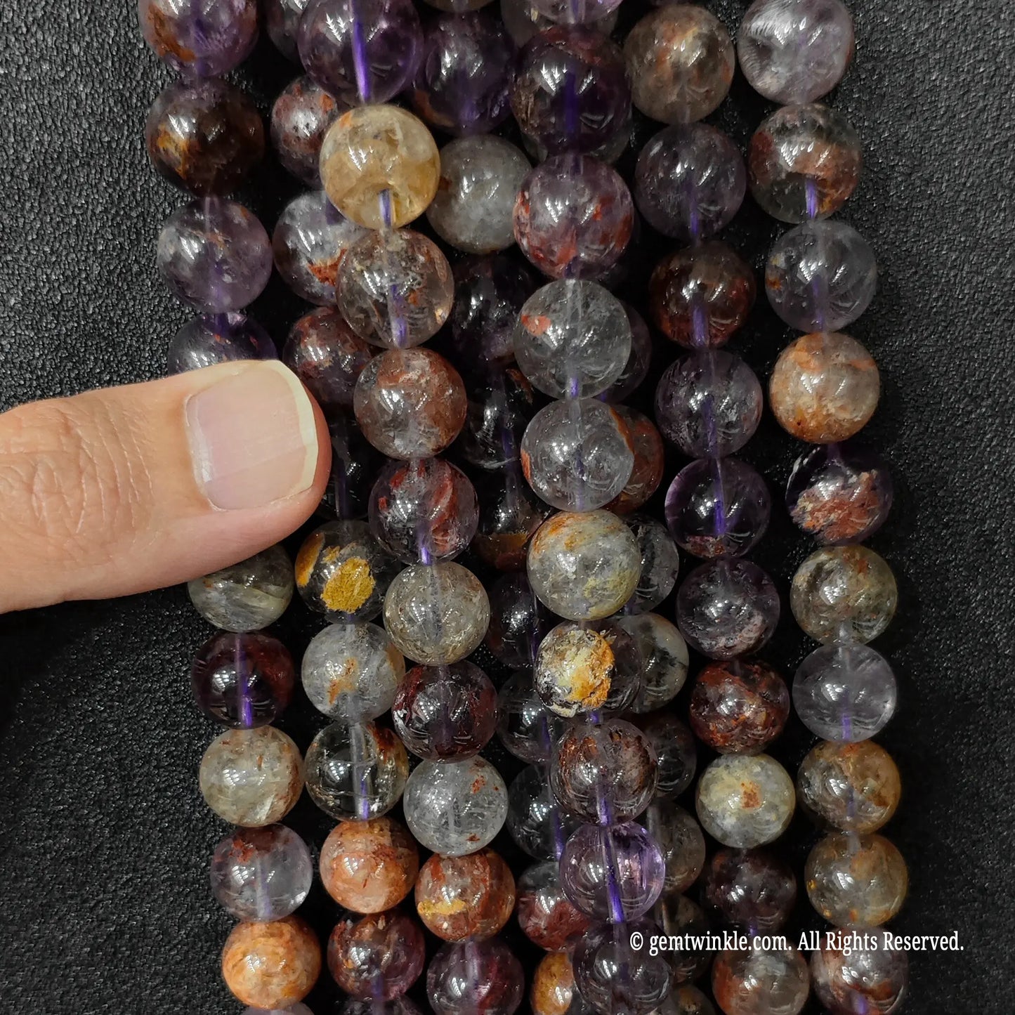 Raw purple crystal beads in progressive six to fourteen millimeter sizes being displayed by hand for scale verification