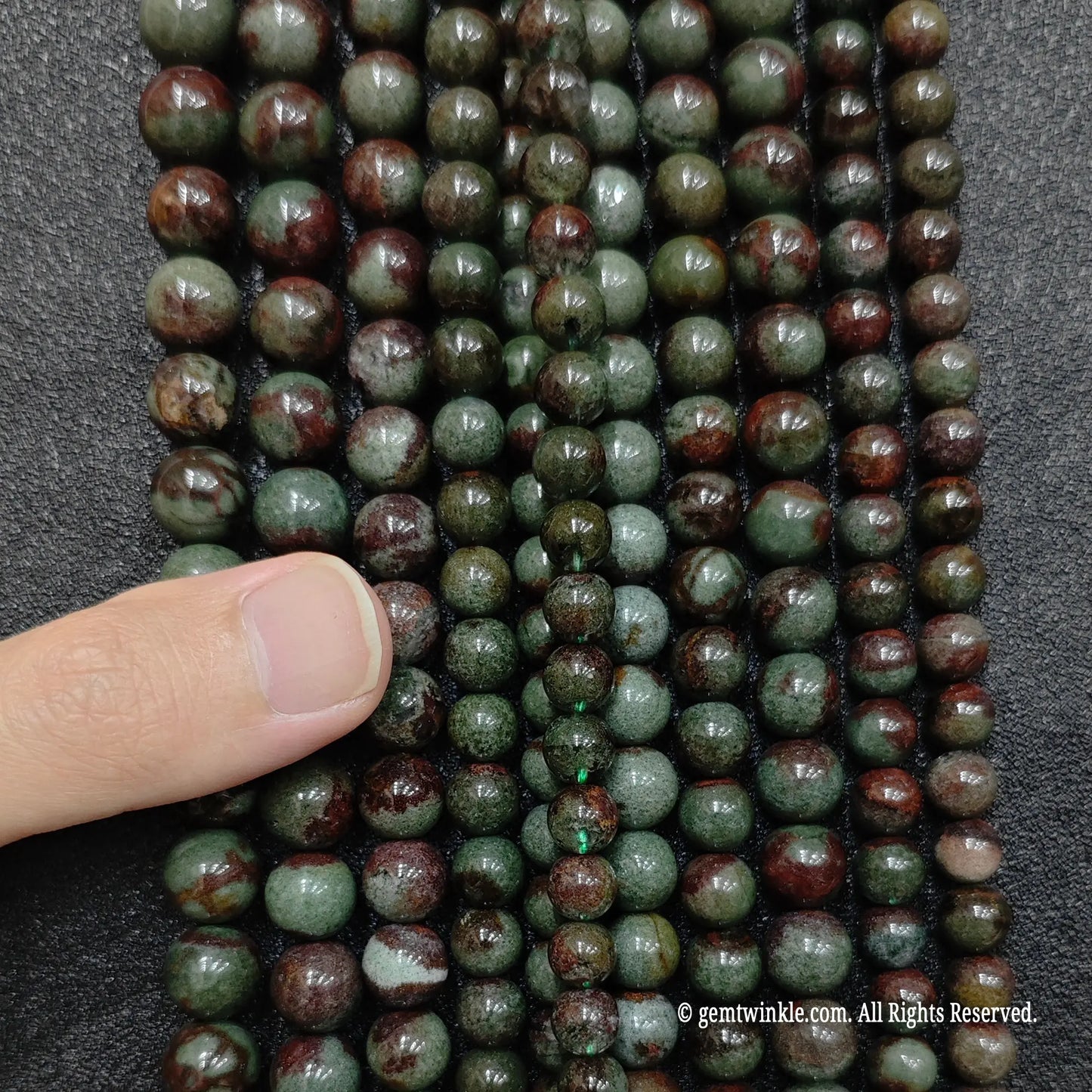 hand showing vertical strands of green phantom quartz crystal beads for size comparison