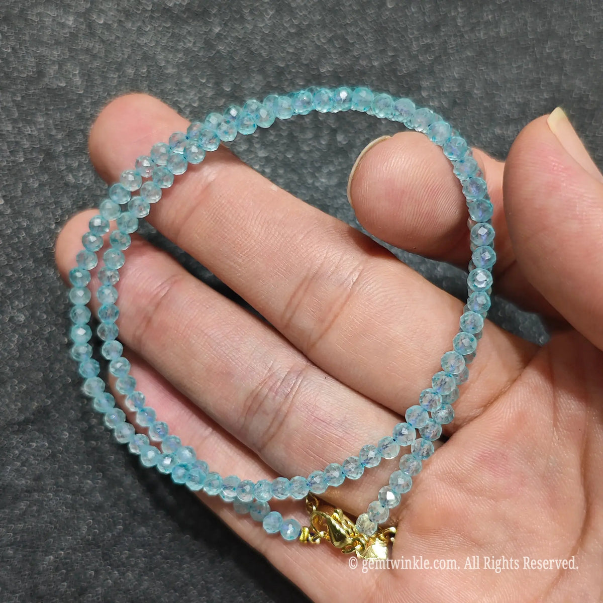 Close up of 3mm faceted sky blue topaz beads looped on hand highlighting gold-toned extension hardware