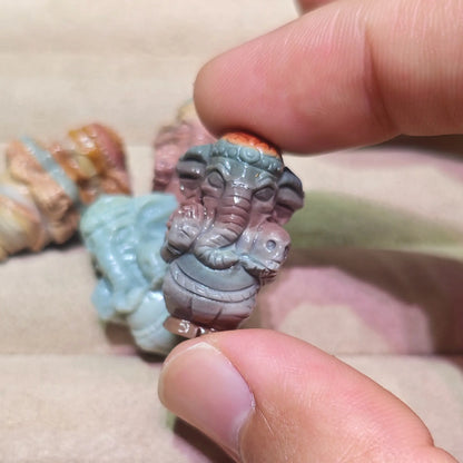 slate gray carved ganesha statue held in fingers close up with other color variations in background