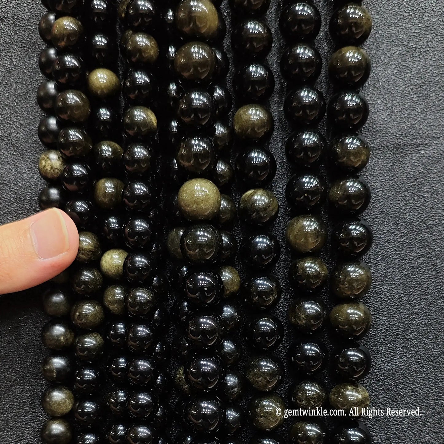 Hand holding multiple strands of natural gold sheen obsidian crystal beads for quality and scale check
