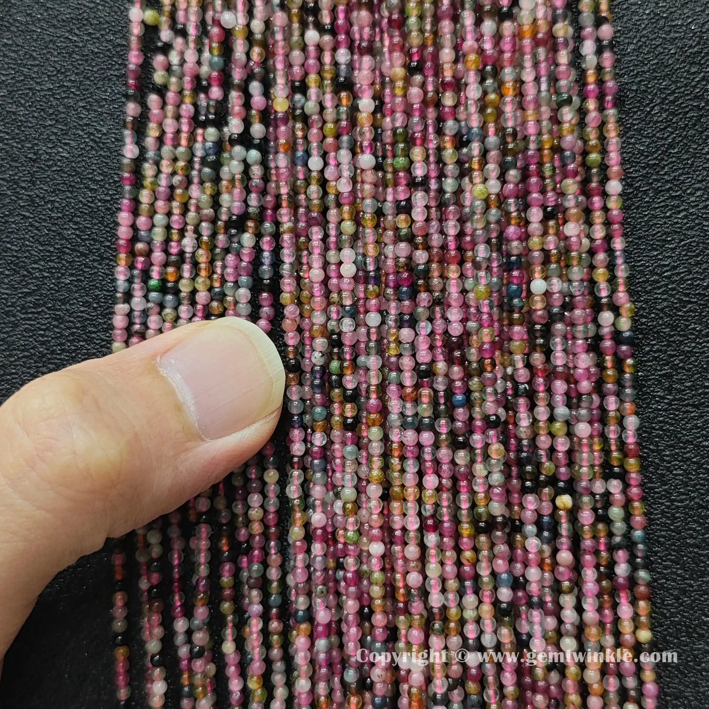 Finger holding small semi translucent multi color tourmaline bead strands demonstrating scale for jewelry makers