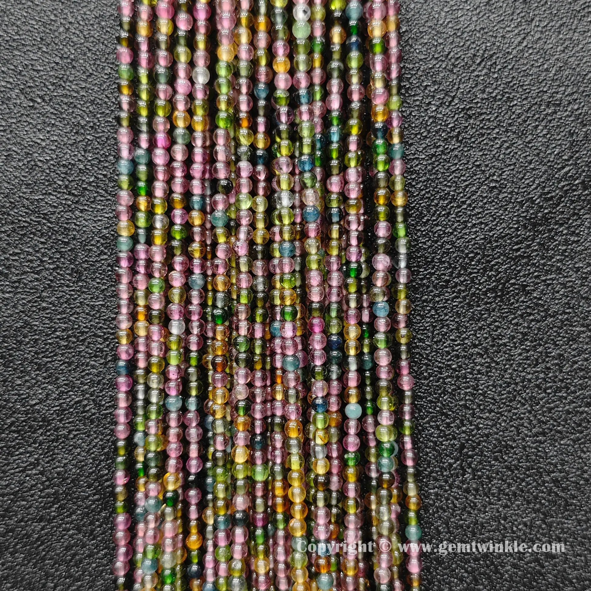 Finger holding small Grade B multi color tourmaline 2.5mm petite bead strands demonstrating scale