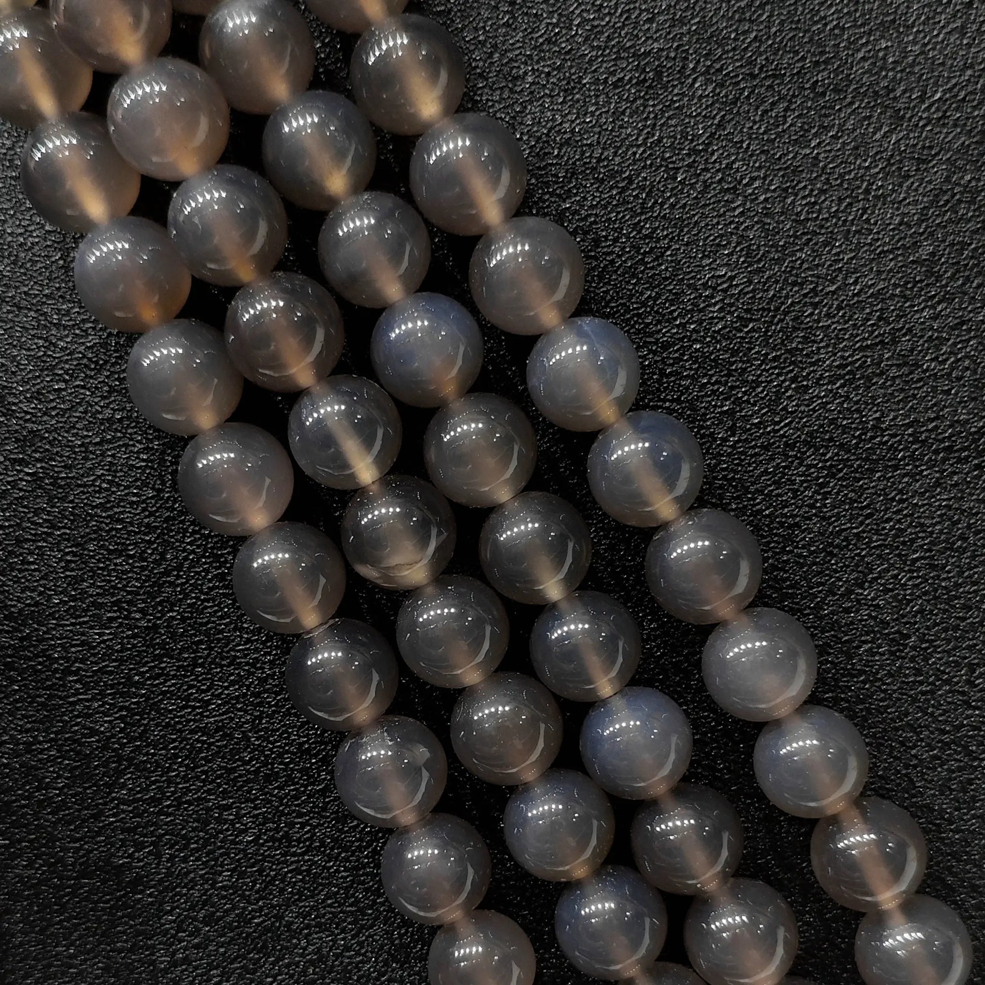 Close up view of three high gloss smoky grey agate smooth round beads strands showcasing misty translucent tones over a genuine natural base in image_bd33c9.jpg