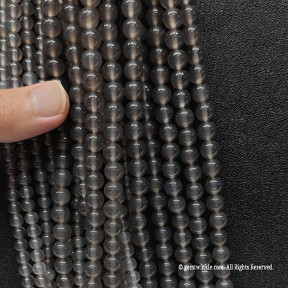 A large bundle of small smoky grey crystal round beads held in hand for studio size density verification