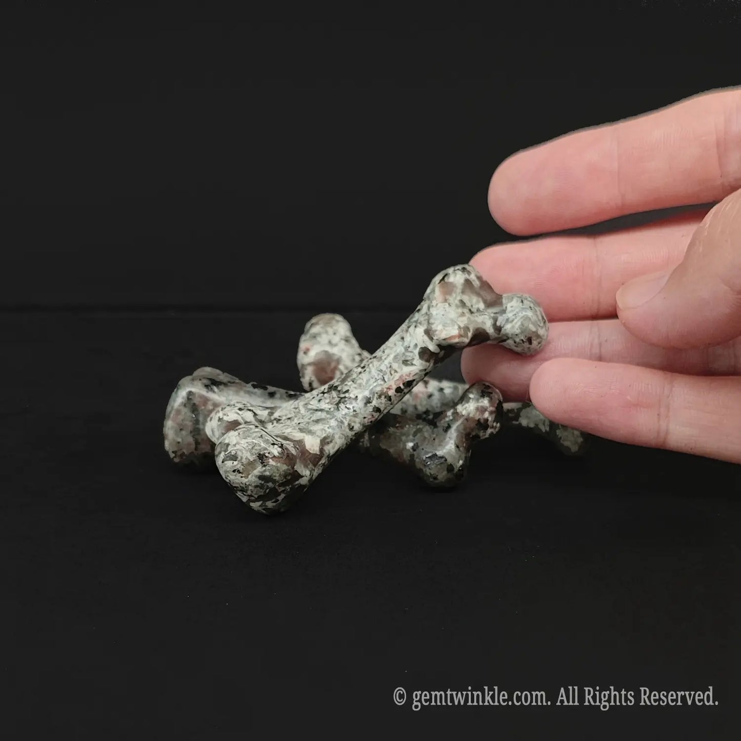A tactile grey jasper specimen bone carving resting on a dark surface for witchy room styling