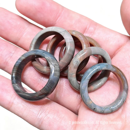 Assorted solid Alashan agate crystal ring bands held in hand highlighting polished finish and natural mineral bandings