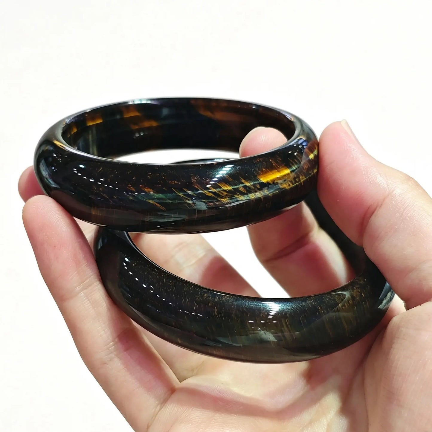 Stacked natural blue tiger eye bangles resting on palm showing high polish and chatoyant light reflections