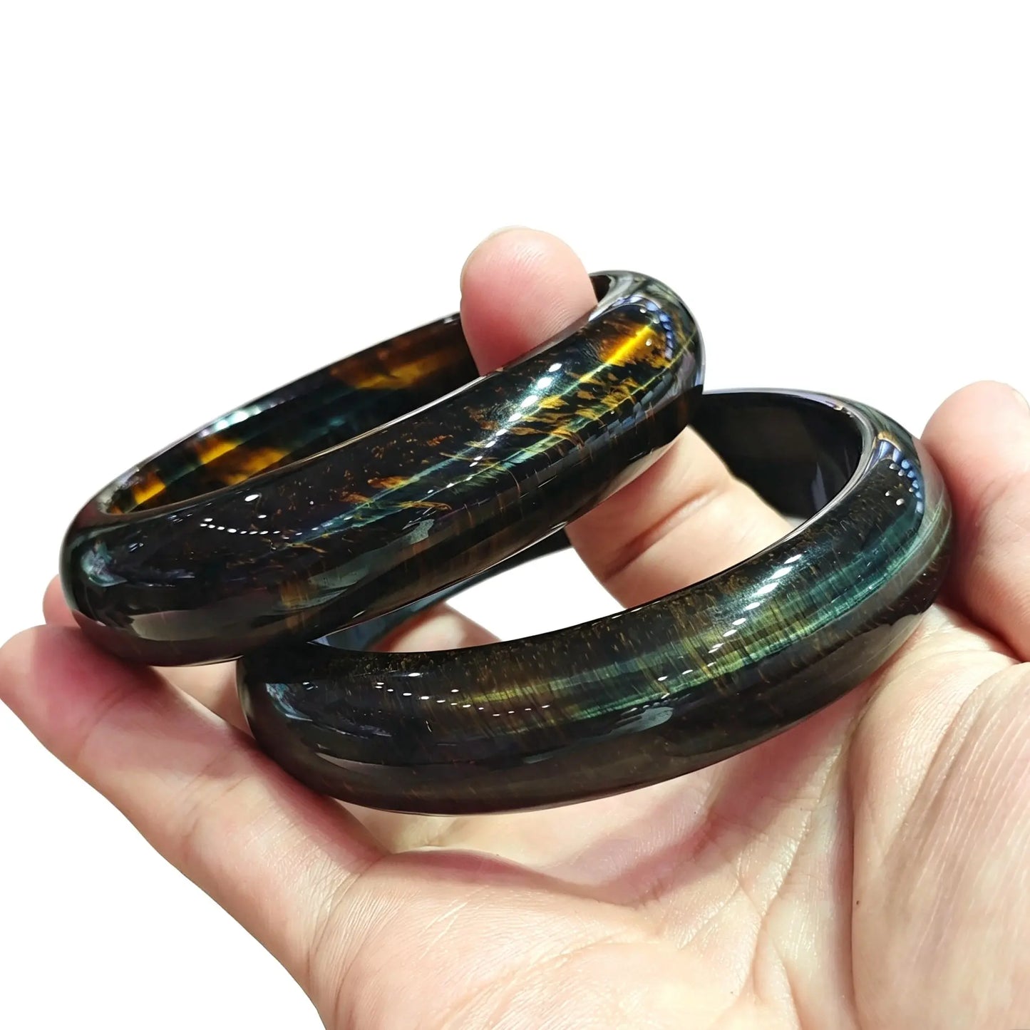 Fingers holding two smooth solid stabilized blue tiger eye bangles displaying silky chatoyancy and golden blue reflections