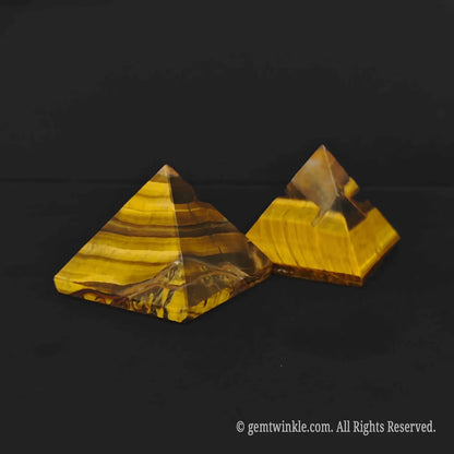 Close up of polished gold tigers eye pyramid showing segmented geometry design on a dark surface