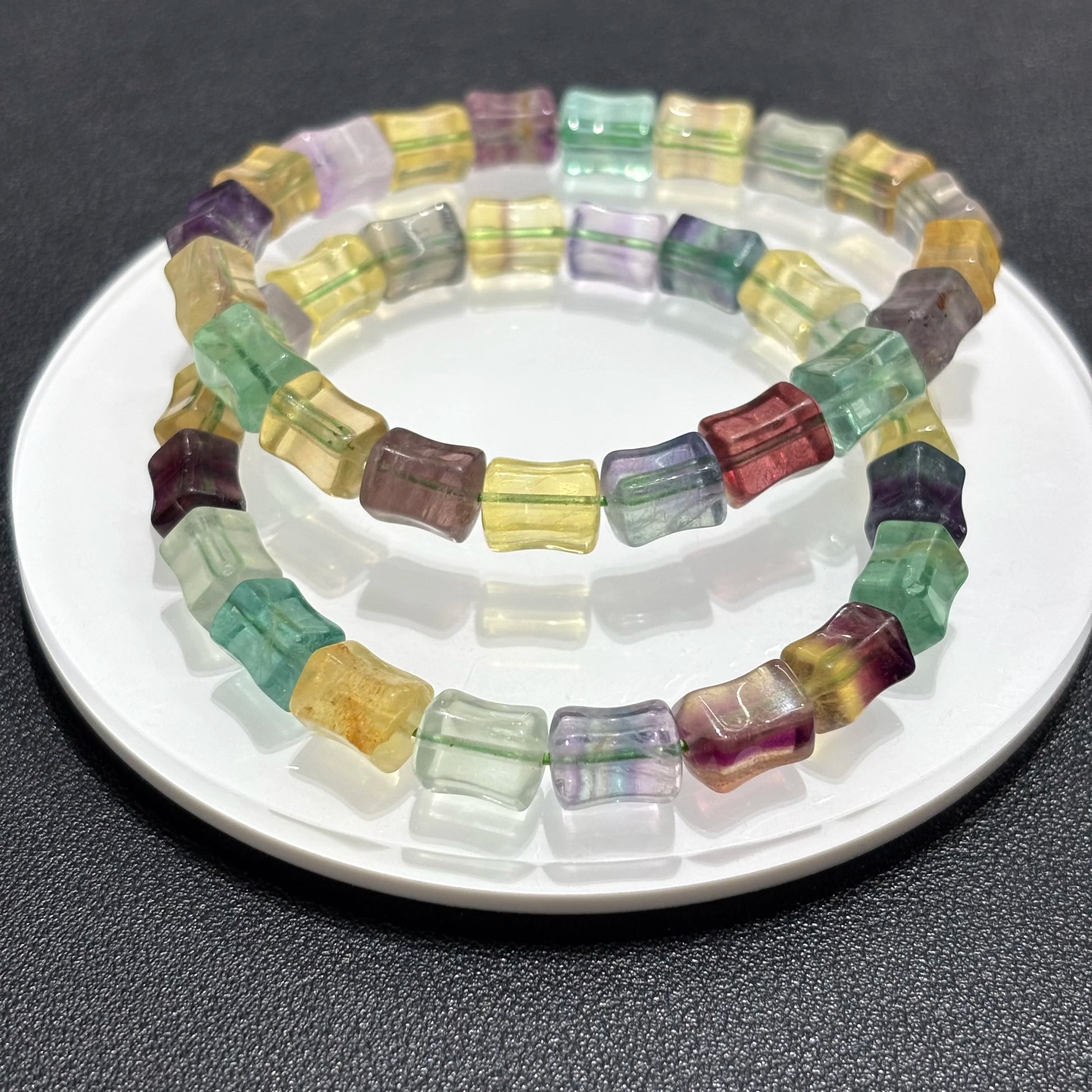 Two natural fluorite square bead bracelets displayed together on a white plate, highlighting the vibrant rainbow colors and bamboo texture.