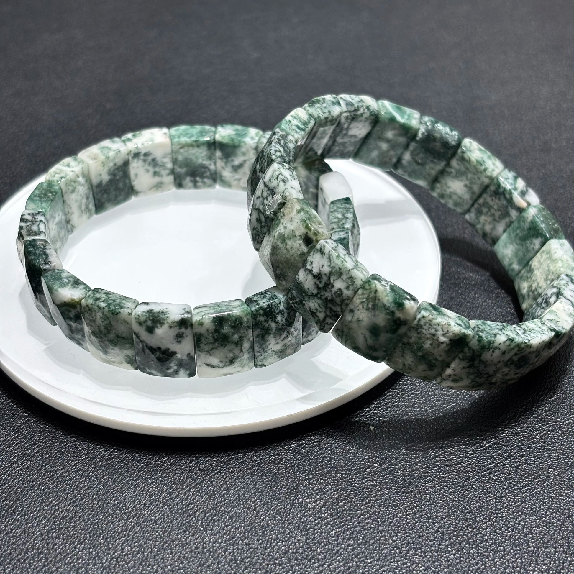 Two natural moss agate square bead bracelets displayed together on a white plate, highlighting the unique green patterns in each stone.