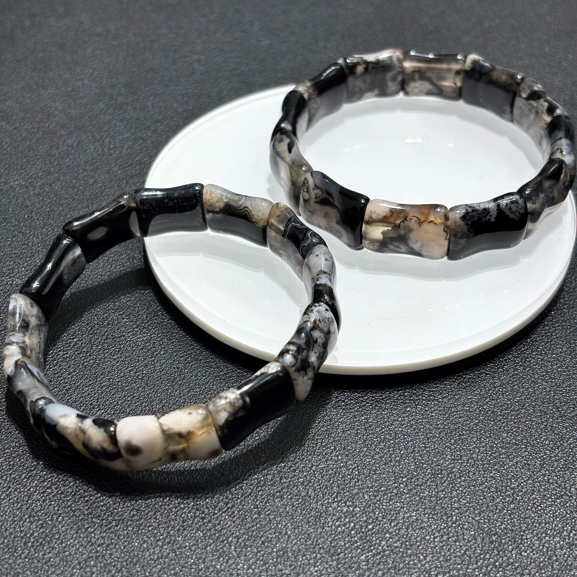 Stacked view of black sakura agate bamboo bracelets on a plate.