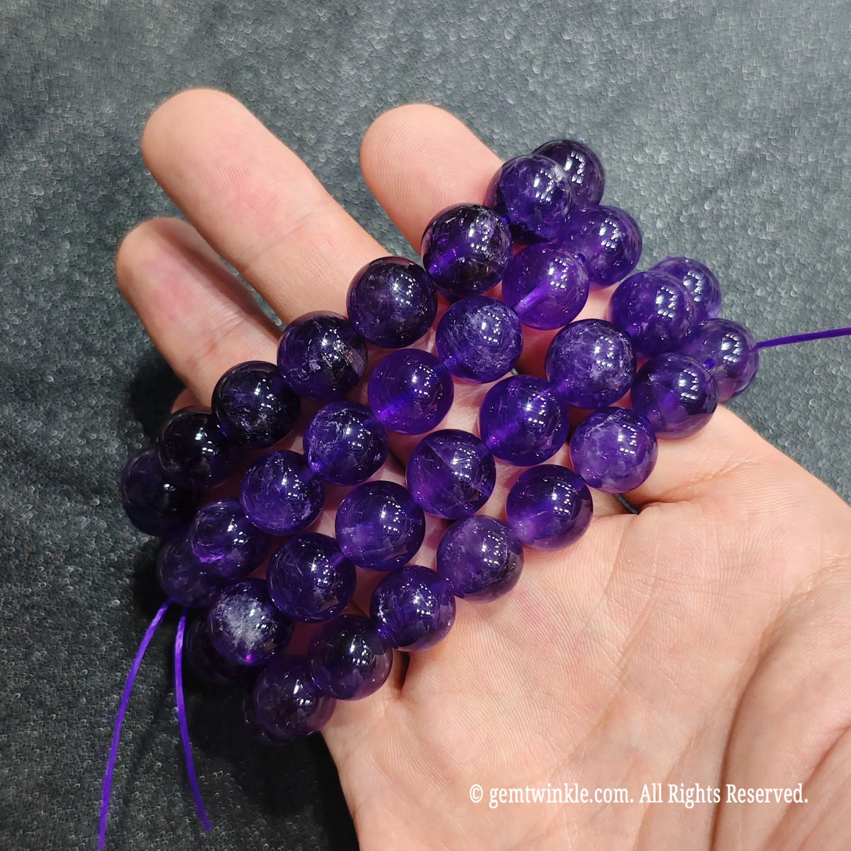 Multiple strands of deep purple amethyst wristlets held on hand illustrating natural bead-to-bead color intensity