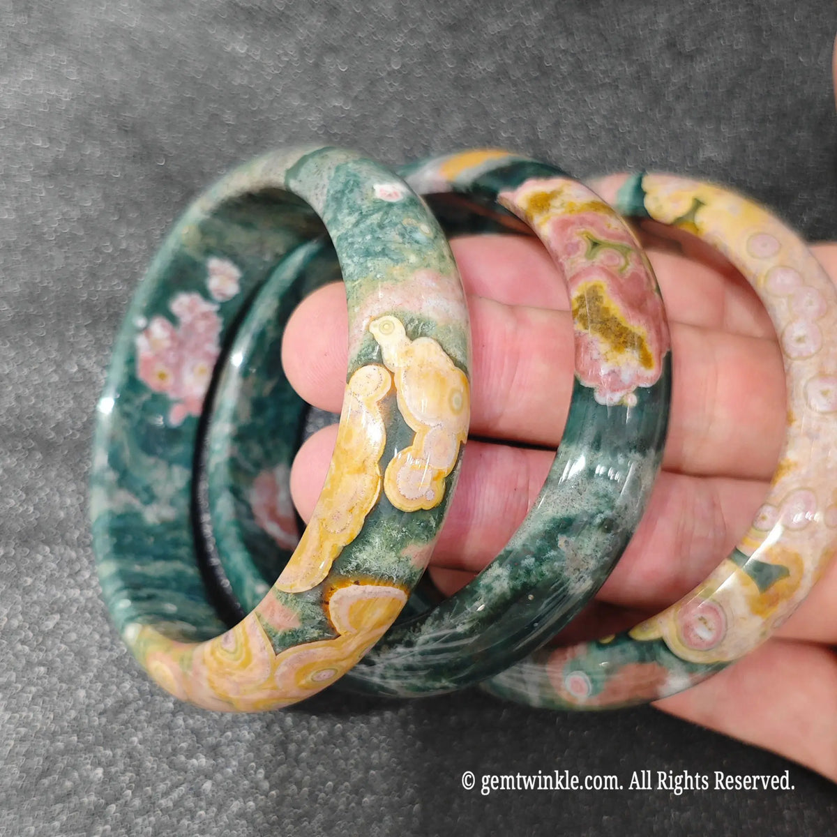 Stacked view of natural ocean jasper stone bangles displayed on hand under ambient studio lighting